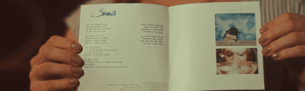 Na imagem, Luiza segura um um livreto com a letra da música Sinais.